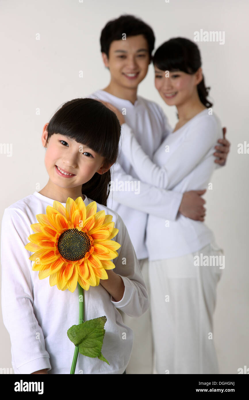 Oriente famiglia asiatica con un bambino, i genitori abbracciando, figlia tenendo il girasole, sorridente, guardando la fotocamera Foto Stock