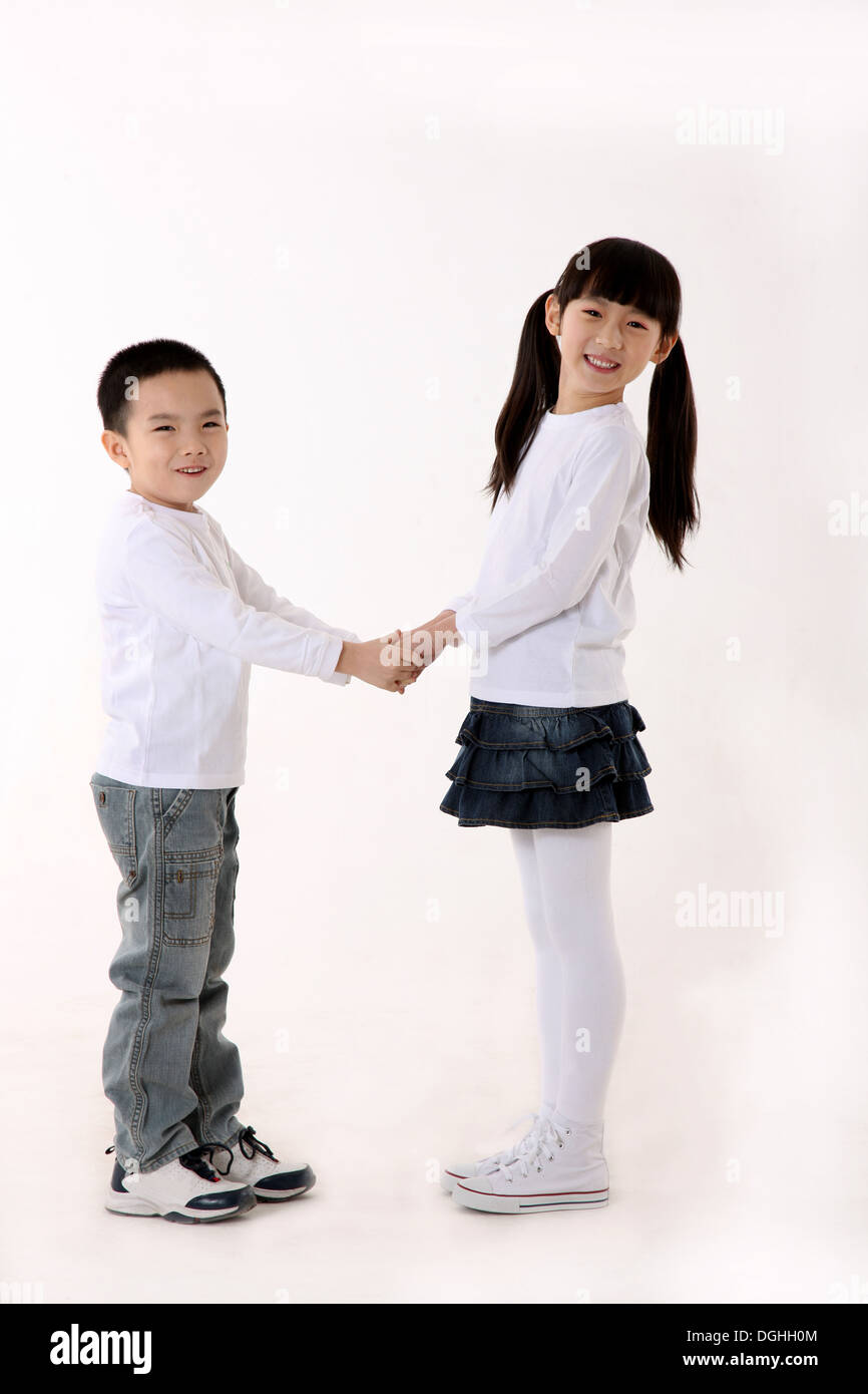 East Asian un ragazzo e una ragazza in piedi sul pavimento, mano nella mano, sorridente, guardando la telecamera Foto Stock