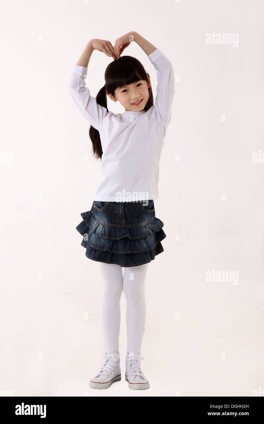 Oriente ragazza asiatica in piedi sul pavimento, mettendo a forma di cuore, guardando la fotocamera con un sorriso Foto Stock