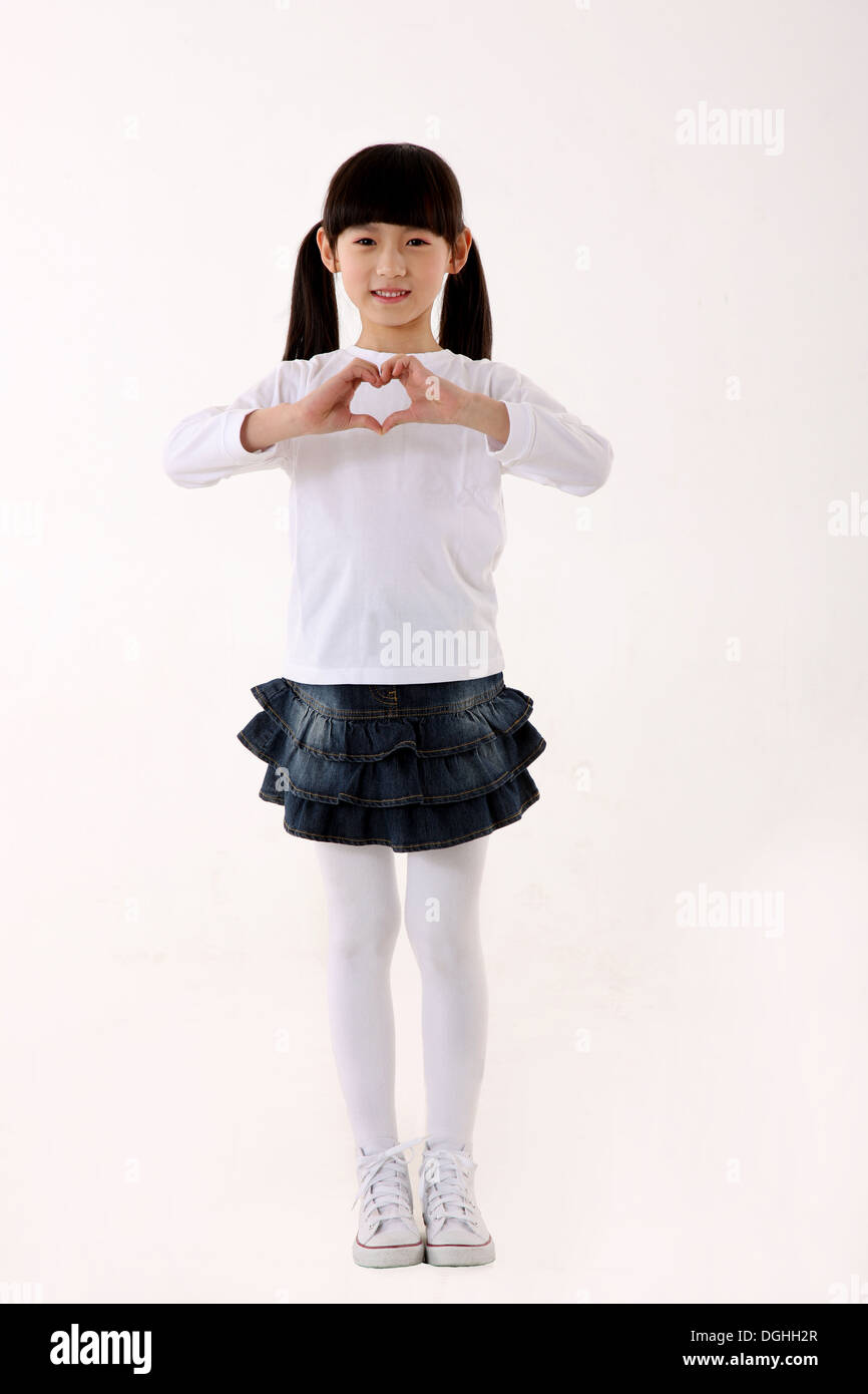 Oriente ragazza asiatica messa a forma di cuore, guardando la telecamera con un sorriso, in piedi sul pavimento Foto Stock