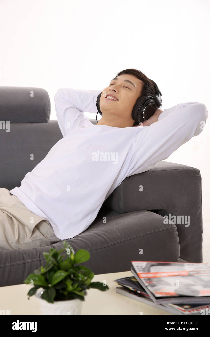 East Asian dell'uomo uno stile di vita informale, uomo in bianco abiti casual sdraiato sul divano ascoltando la musica Foto Stock