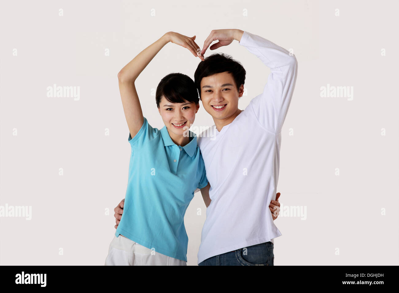 East Asian giovane standing, abbracciando, mettendo a forma di cuore, sorridente e guardando la fotocamera Foto Stock