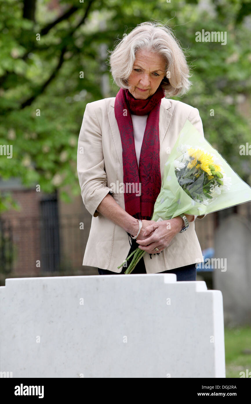 Senior donna azienda fiori nel cimitero Foto Stock