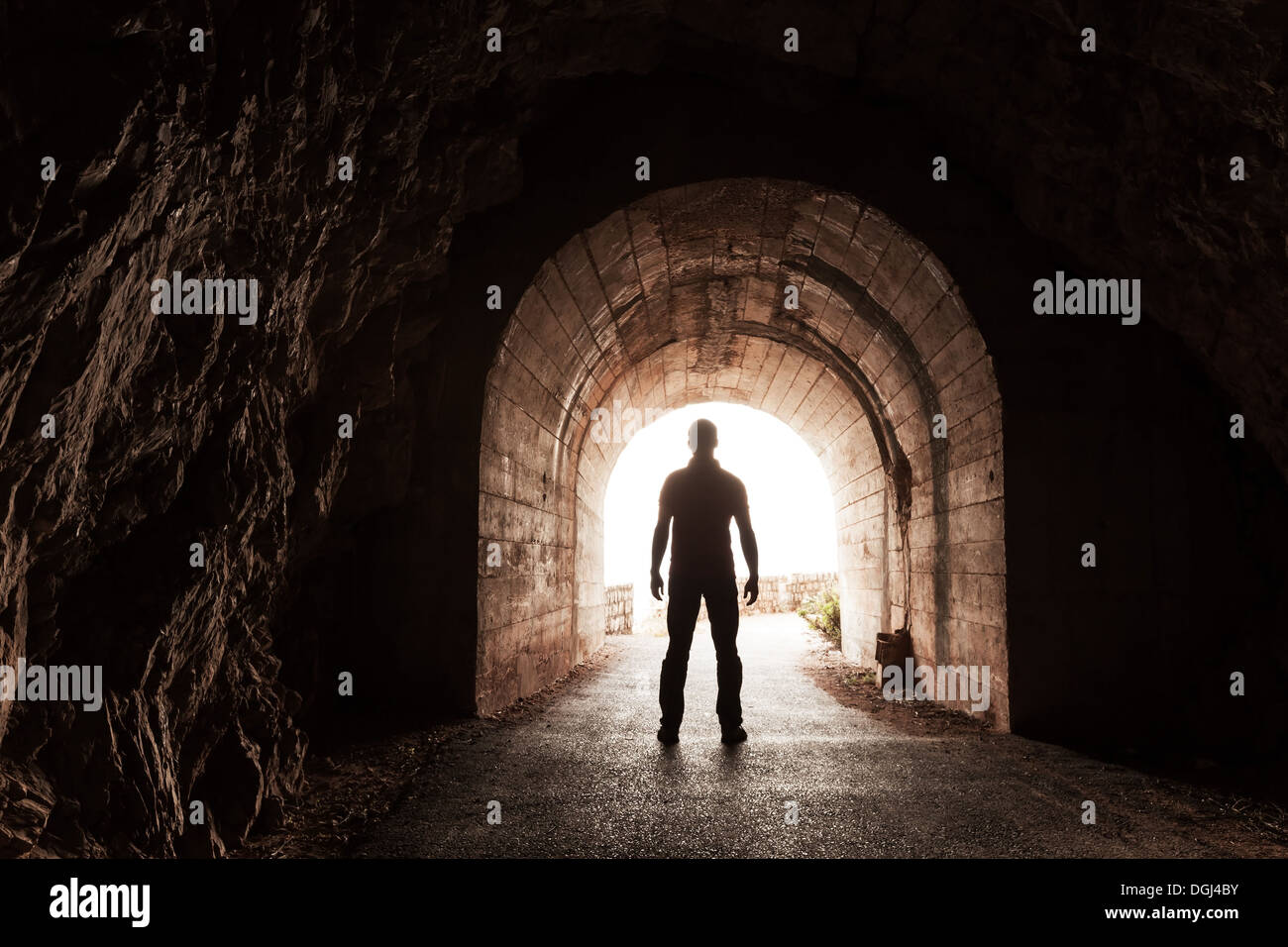 Giovane uomo sorge nel buio del tunnel di cemento e si affaccia nel finale incandescente Foto Stock