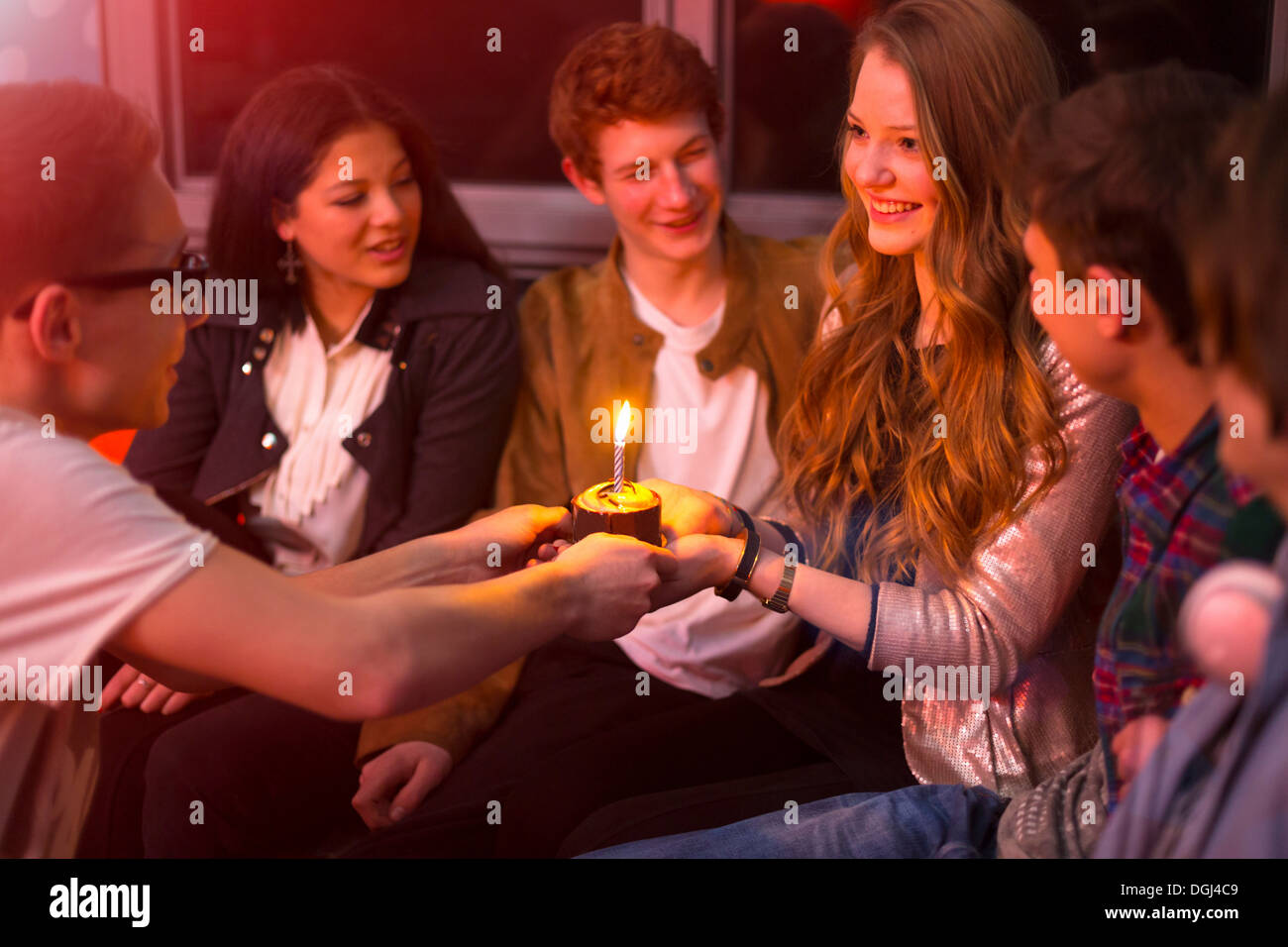 Gruppo di adolescenti seduti intorno a torta di compleanno Foto Stock