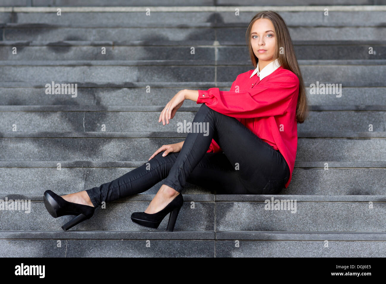 Giovane donna che indossa un top rosso, nero jeans e tacchi alti in posa  mentre è seduto sulle scale Foto stock - Alamy