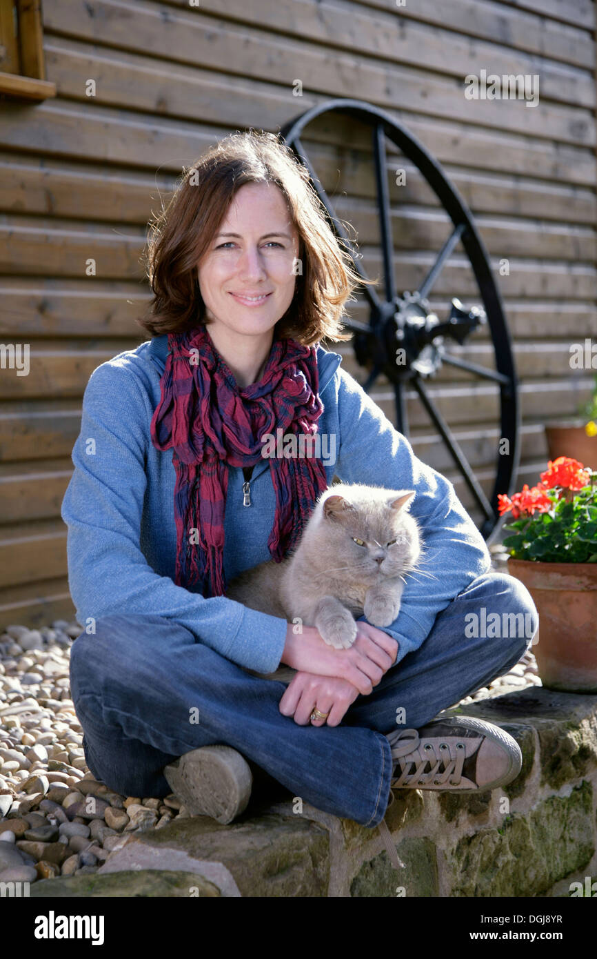 Giovane donna seduta su una parete con un gatto grigio sul suo grembo. Foto Stock
