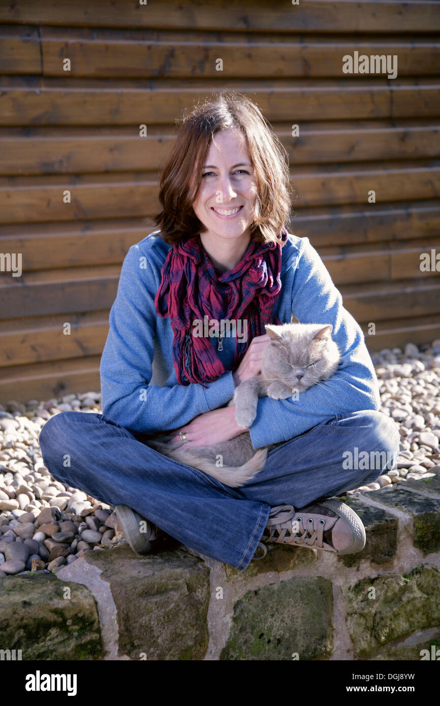 Giovane donna seduta su una parete con un gatto grigio sul suo grembo. Foto Stock