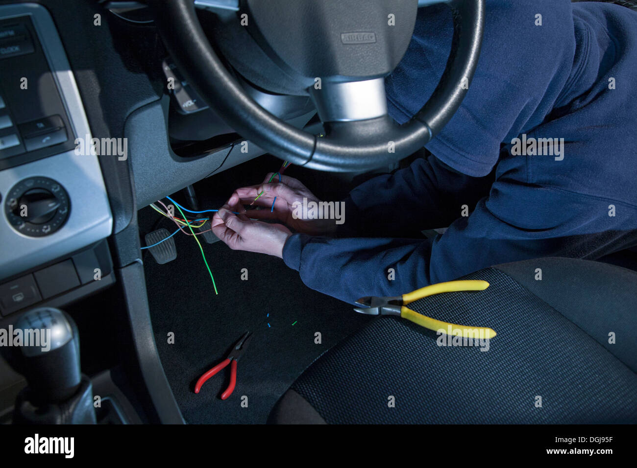 Un uomo che indossa una felpa con cappuccio cablaggio a caldo di un'auto. Foto Stock