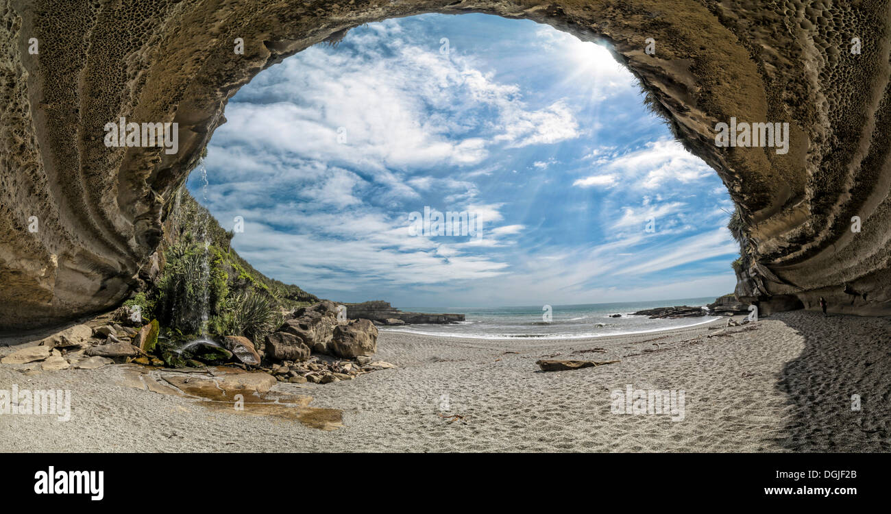 Donna vagare attraverso il potente rock sovrasti di Truman's Cove sulla spiaggia con una cascata, Te Miko, Trumans Bay Foto Stock