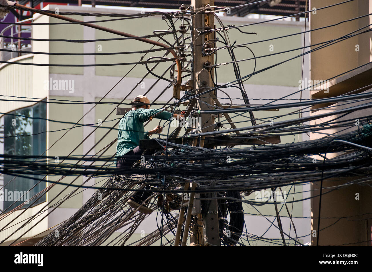 Un Thai ingegnere telefono installando un cavo su un palo del telegrafo in una strada a Bangkok. Foto Stock
