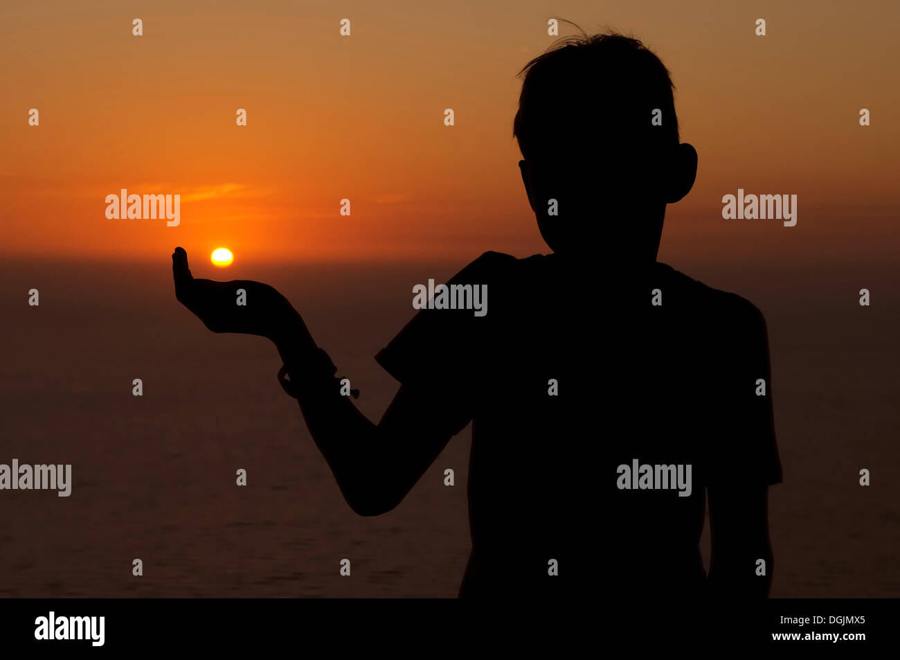 Silhouette di un bambino contro il cielo al tramonto, ragazzo tenendo premuto il sole di setting in mano, Lefkas, Grecia, Europa Foto Stock