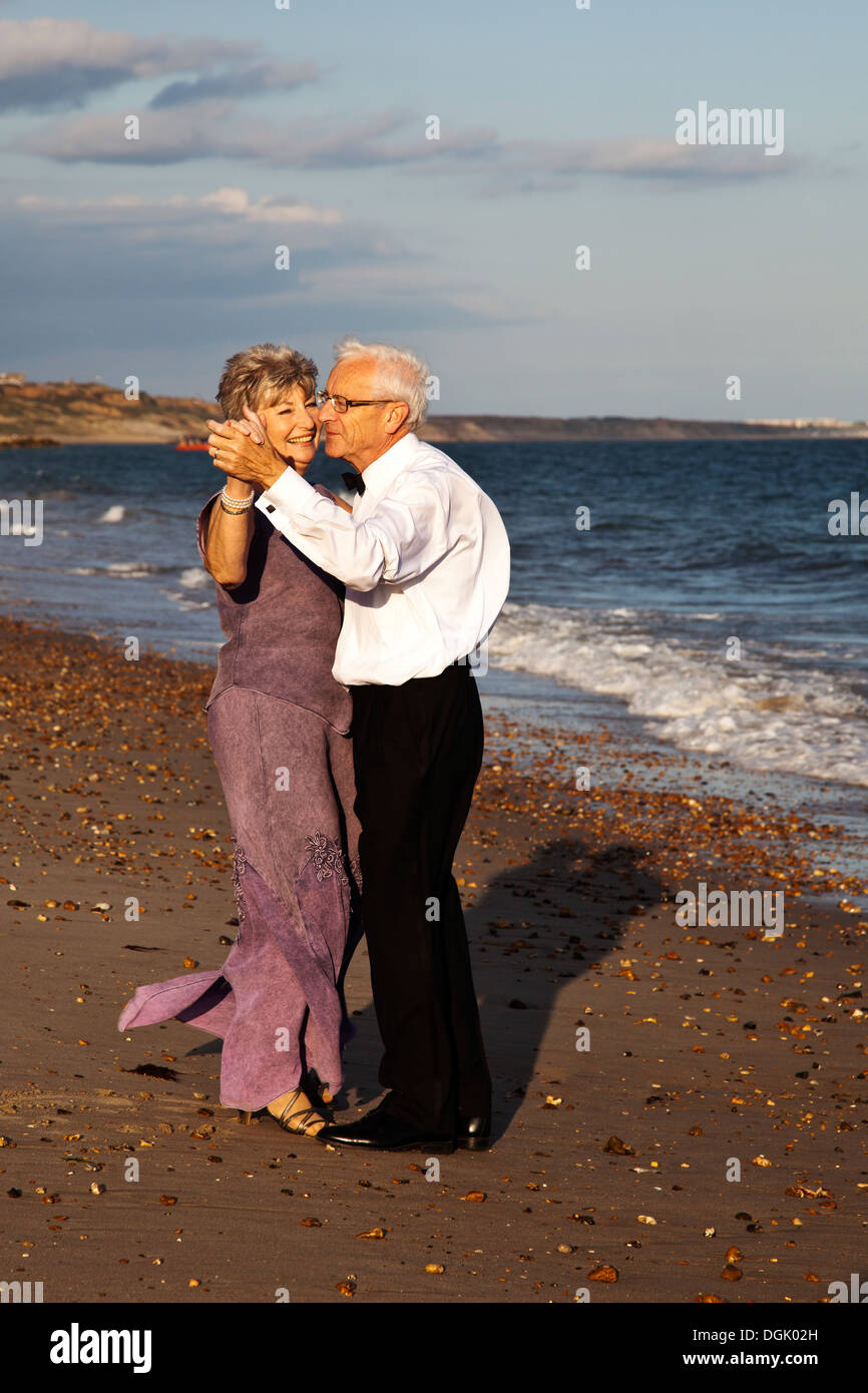 Coppia matura ballando in riva al mare dopo una sera d'estate. Uomo in camicia bianca pantaloni neri, donna nel lungo abito lilla Foto Stock
