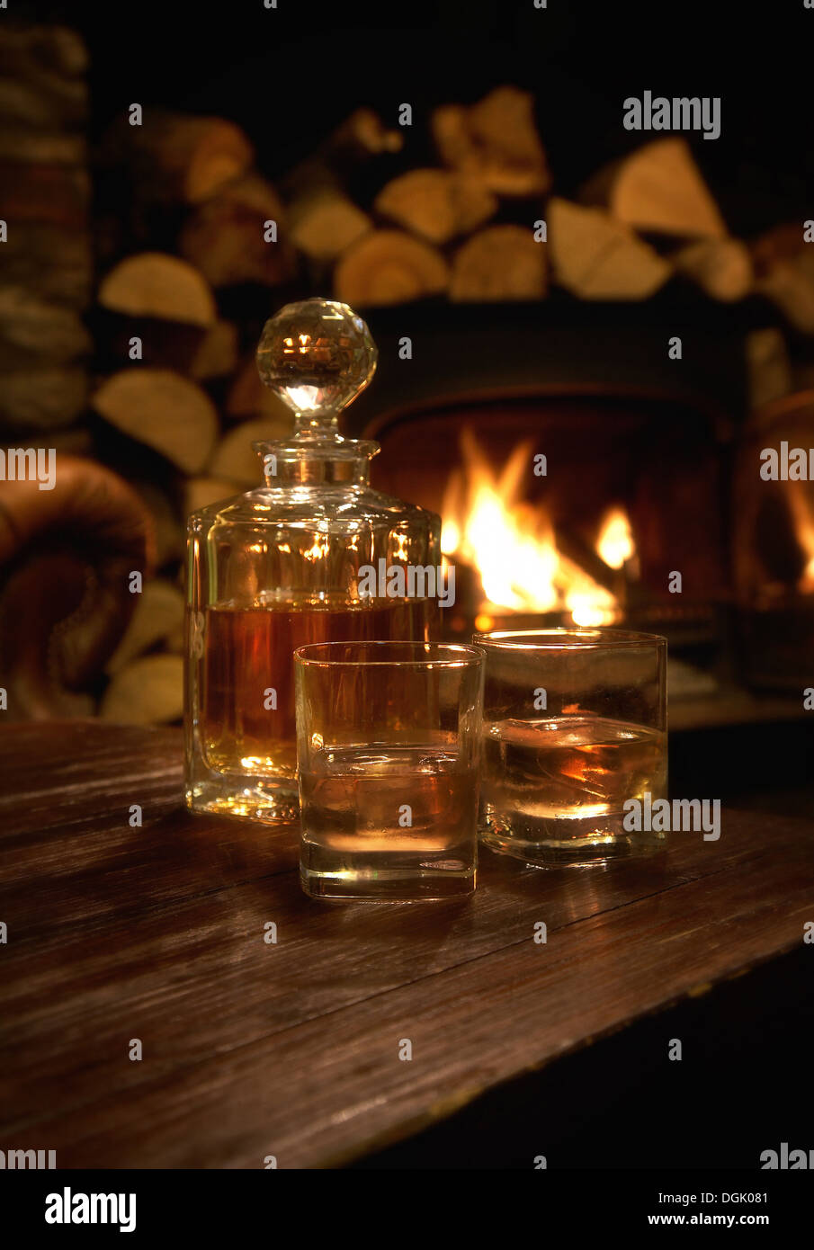 Un decanter e due bicchieri di whisky su una tabella con un fuoco di legna brucia in background. Foto Stock