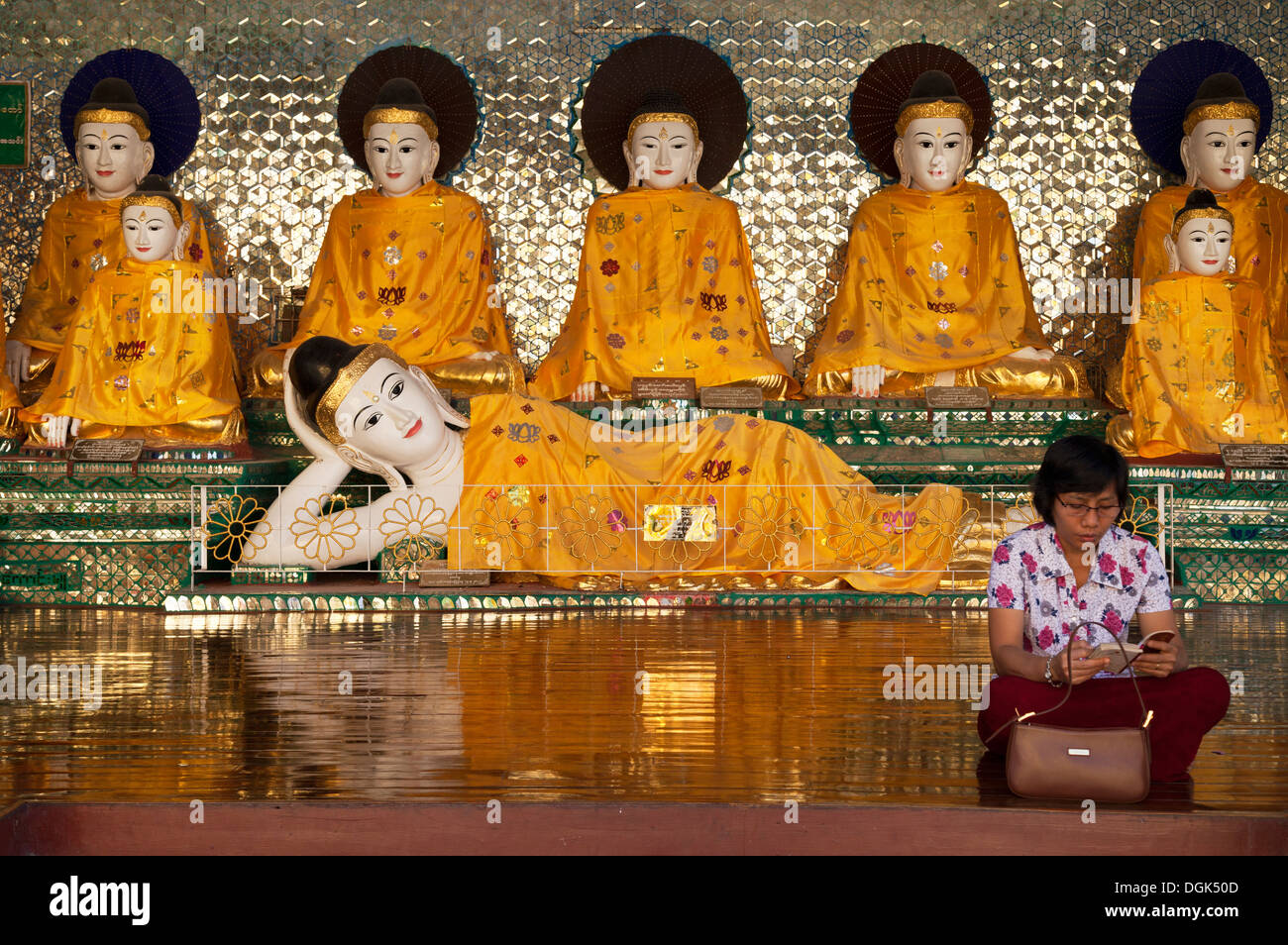 Una donna sutra di lettura di fronte a una schiera di derubato Buddha alla Shwedagon pagoda in Yangon in Myanmar. Foto Stock