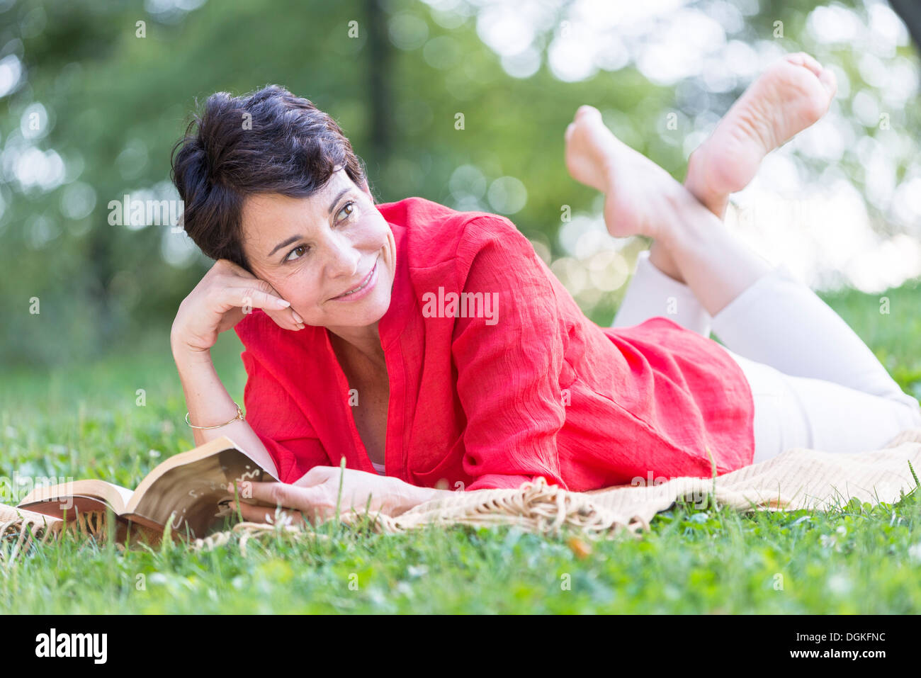 Donna matura giacente su erba e libro di lettura Foto Stock