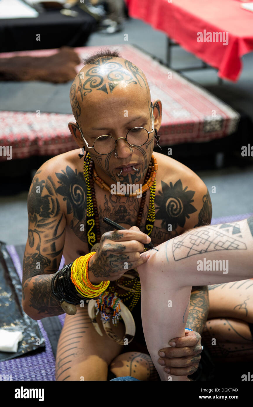 Un tatuaggio indonesiano artista inizia a tracciare un disegno su un uomo del braccio al London International Tattoo Convention. Foto Stock