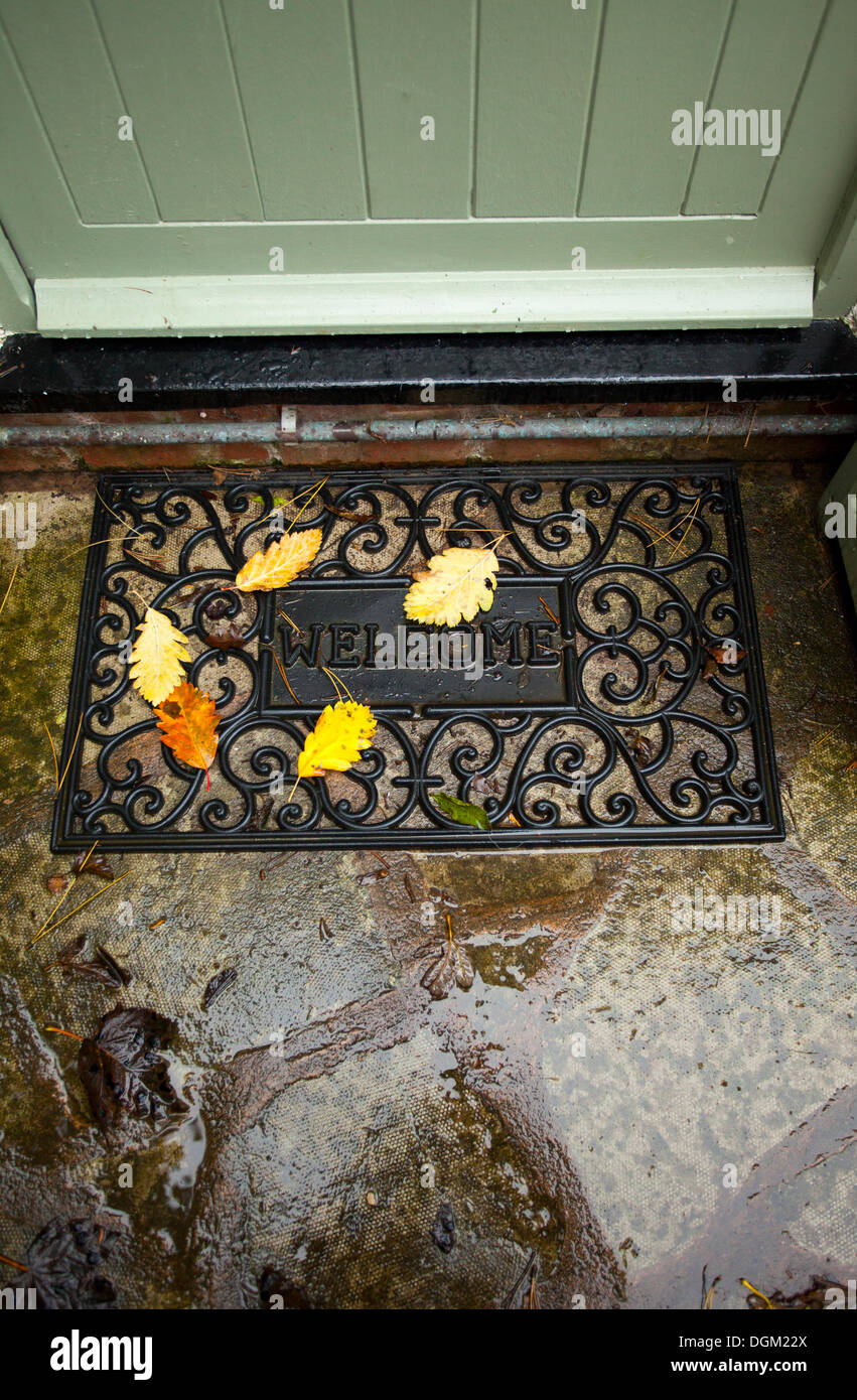 Colori d'autunno foglie che sono caduti su di un tappeto di benvenuto al di  fuori di un cottage porta con le parole benvenuti sul tappetino Foto stock  - Alamy