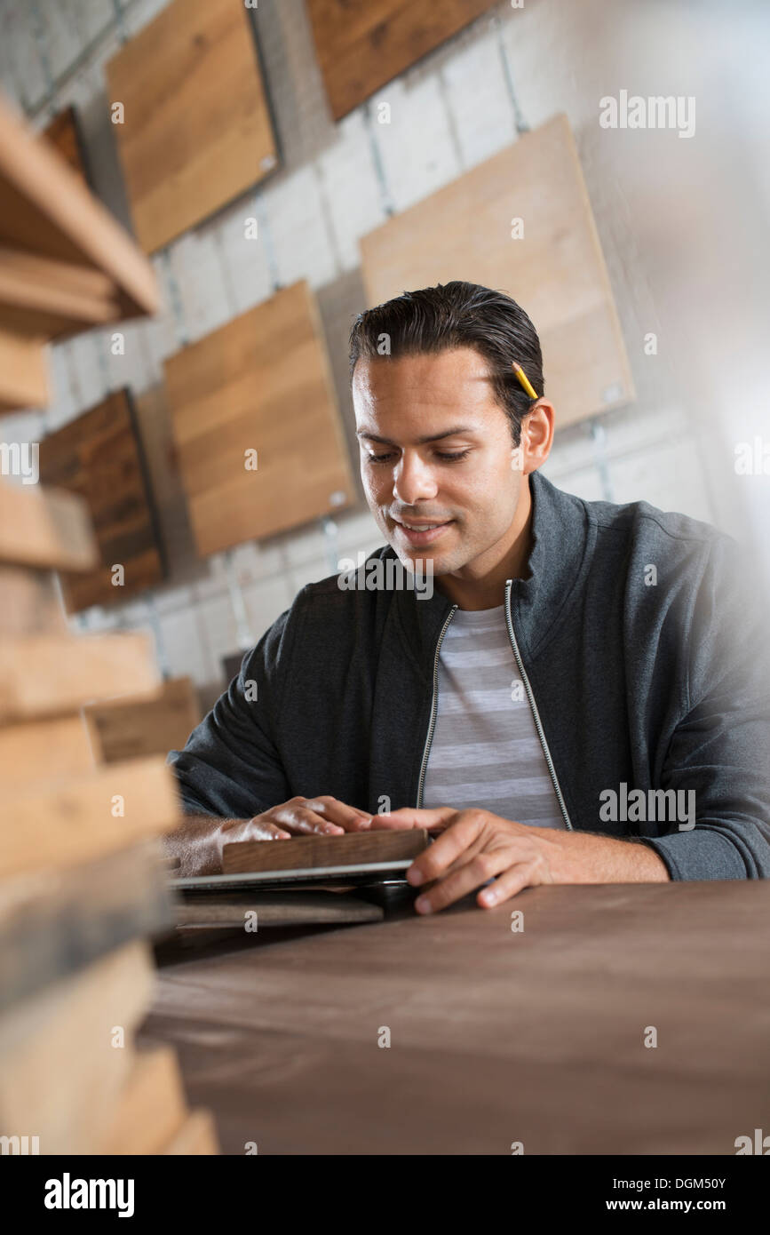 Un giovane uomo in un laboratorio che utilizza materiali riciclati e rigenerati legname a creare mobili e oggetti. Foto Stock