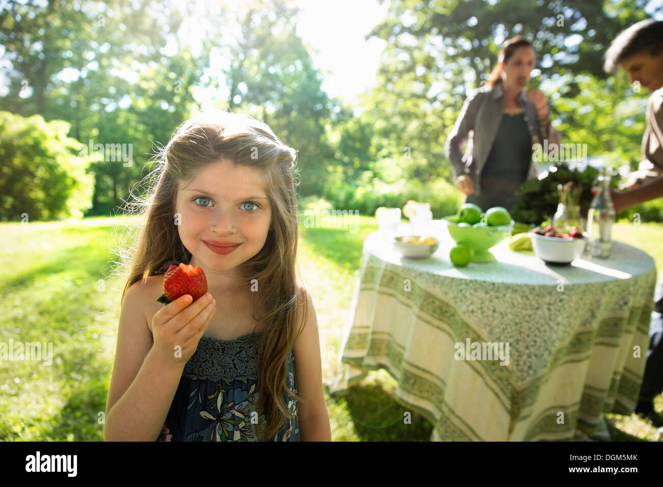 Una giovane ragazza con un grande organicamente fresche prodotte fragole. Due adulti accanto a una tavola rotonda. Foto Stock