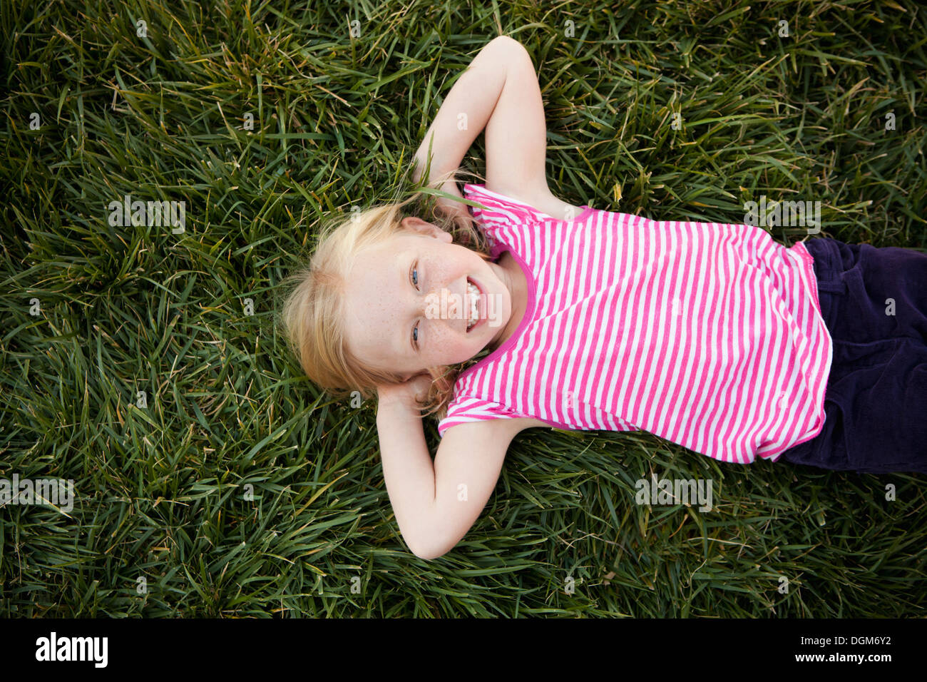 Una giovane ragazza sdraiata su erba le mani dietro la testa sorridente guardando la fotocamera vista da sopra Foto Stock