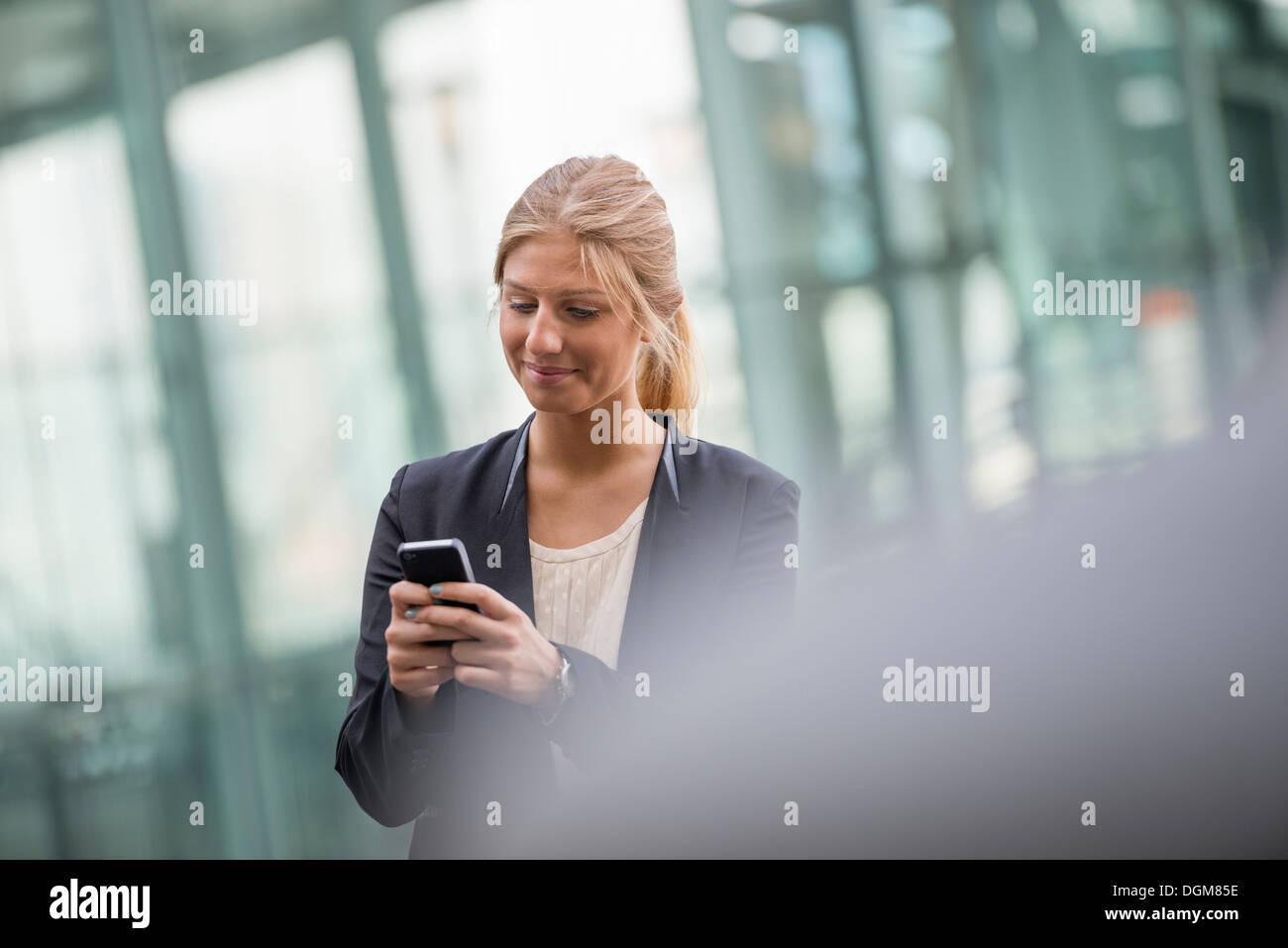 Una bionda e giovane imprenditrice su una città di New York Street. Indossa una giacca nera. Utilizzando un telefono intelligente. Foto Stock