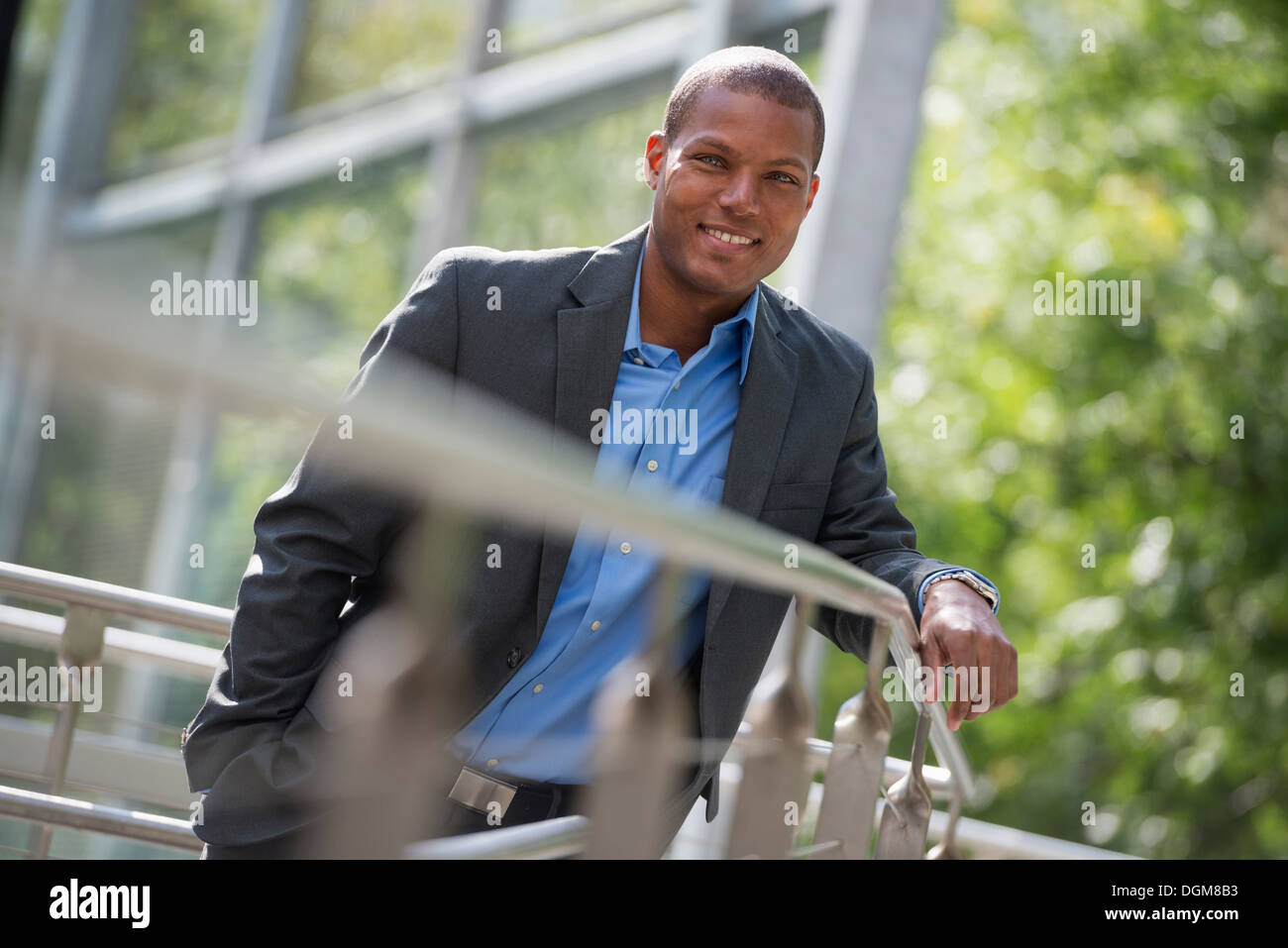 Un giovane uomo in una camicia e a collare aperto maglietta blu, poggiando su una ringhiera in un parco cittadino in estate. Guardando la telecamera. Foto Stock