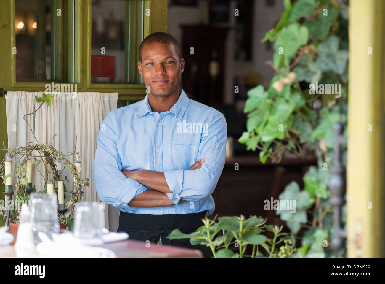 Un uomo in piedi dalla finestra aperta di un cafe bistro o, guardando fuori con i bracci ripiegati. Foto Stock
