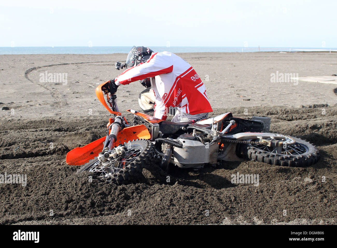 Un pilota di motocross cade con la sua moto sulla sabbia vicino al mare Foto Stock