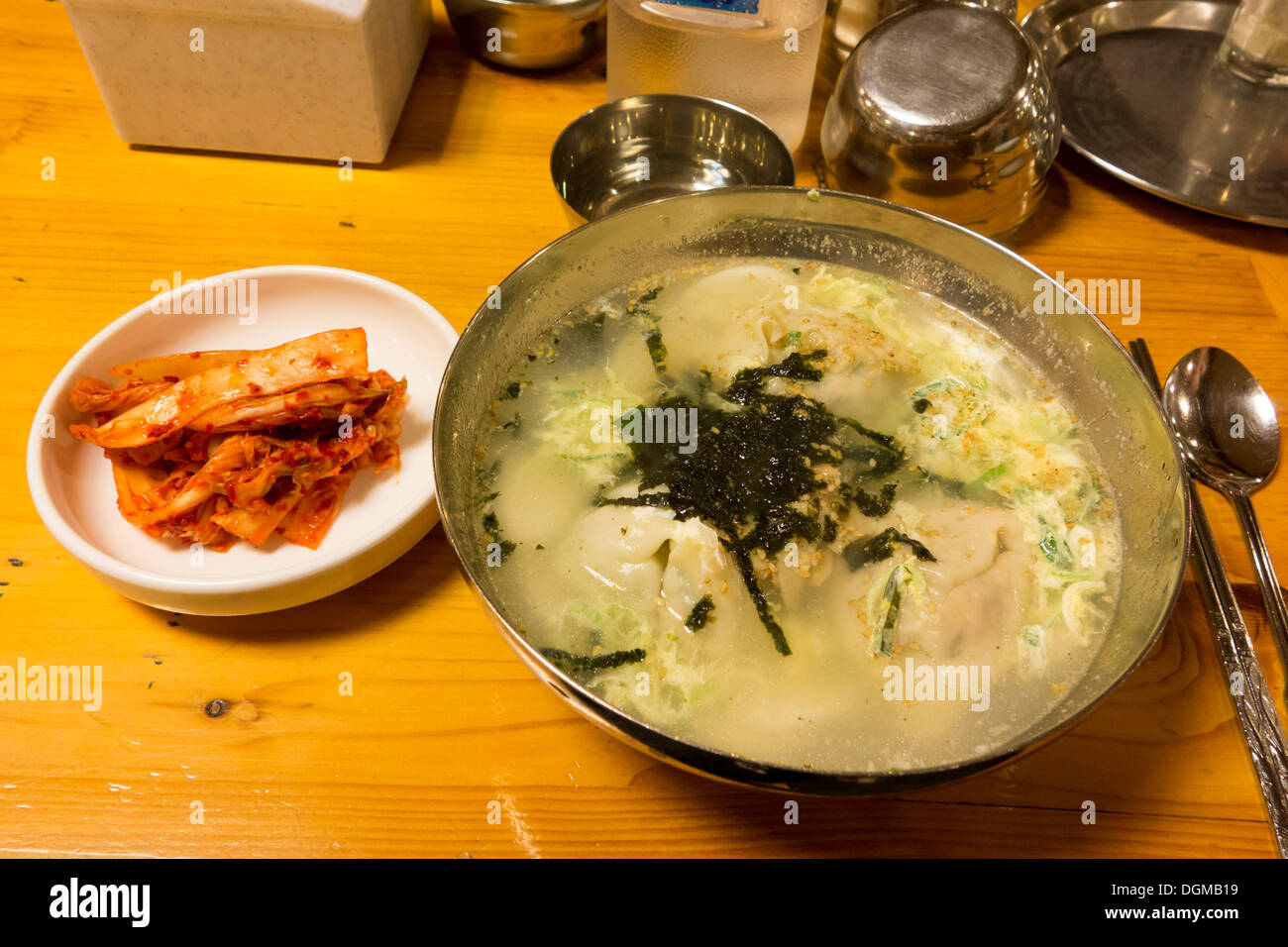 Tteok mandu guk (torta di riso e zuppa di gnocco) in un recipiente in acciaio inossidabile e gimchi su una piccola piastra. Popluar cibo con i coreani. Foto Stock