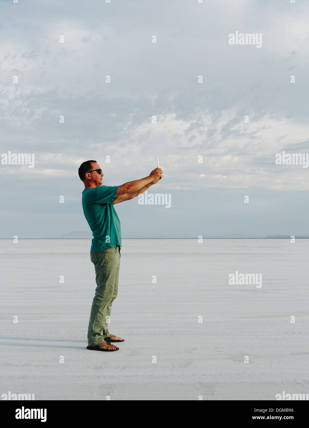 Un uomo in piedi sul Bonneville Saline, scattare una fotografia con dispositivo tablet pc, al tramonto. Foto Stock