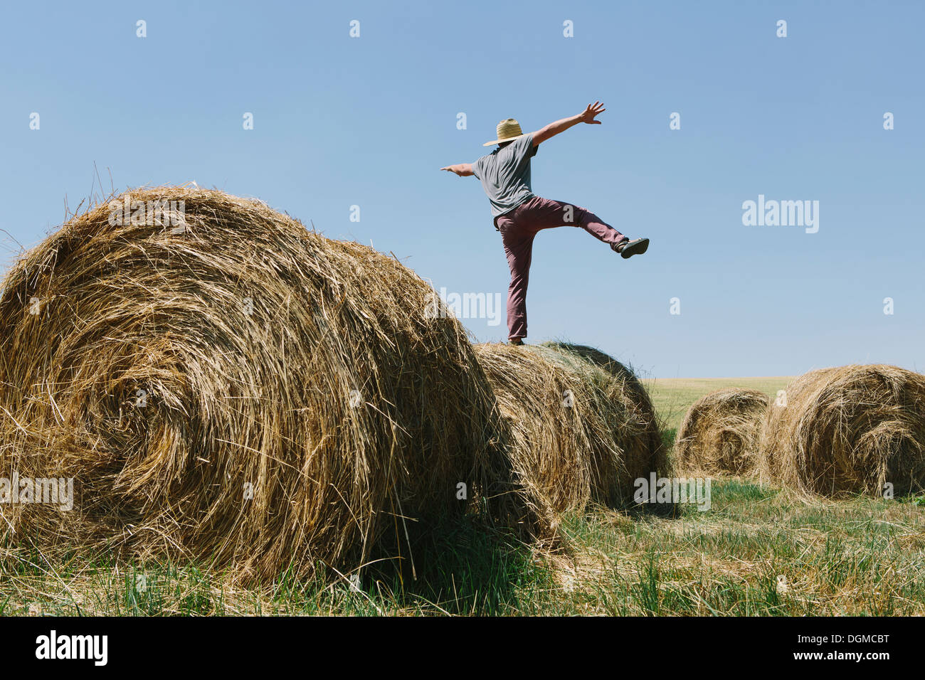 Vista posteriore di un uomo in equilibrio su una gamba sulla parte superiore di una balla di fieno. Foto Stock