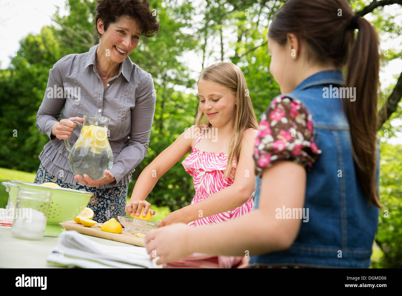 Un estate incontro di famiglia in una fattoria. Una donna e due bambini in piedi fuori da una tabella, che stabilisce la tabella. Facendo una limonata. Foto Stock