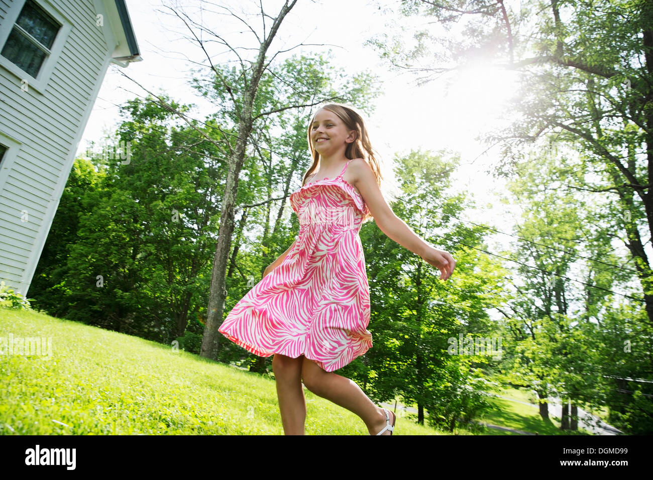 Una giovane ragazza in un rosa sundress modellato in tutta l'erba sotto gli alberi in un casale giardino. Foto Stock