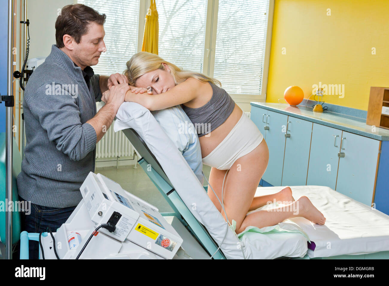 L uomo e la donna nella sala parto durante il parto, la donna in ginocchio sul letto di consegna e di riposo, essa è collegata a un Foto Stock