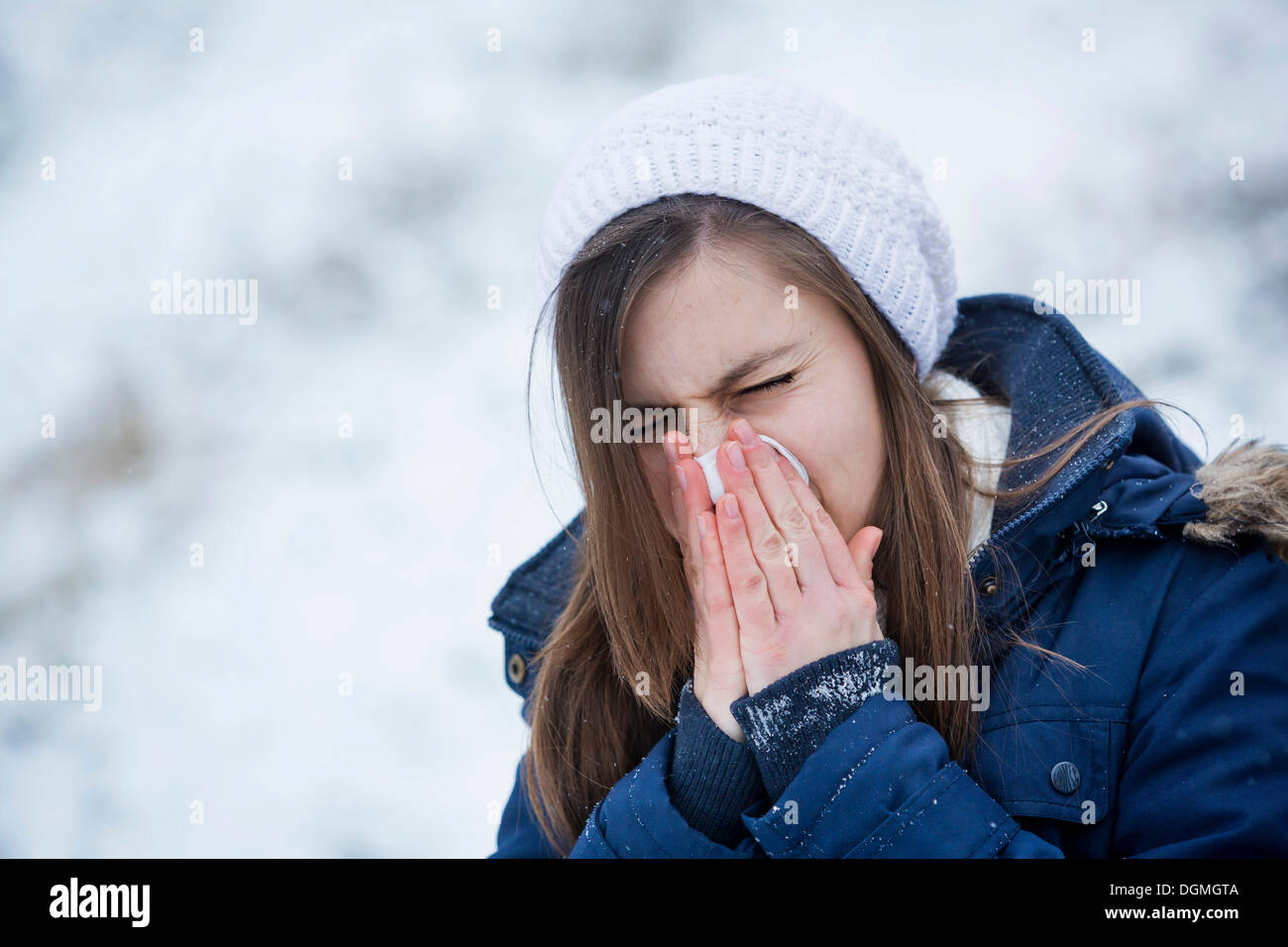 Giovane donna indossa abbigliamento invernale soffia il naso, Germania Foto Stock