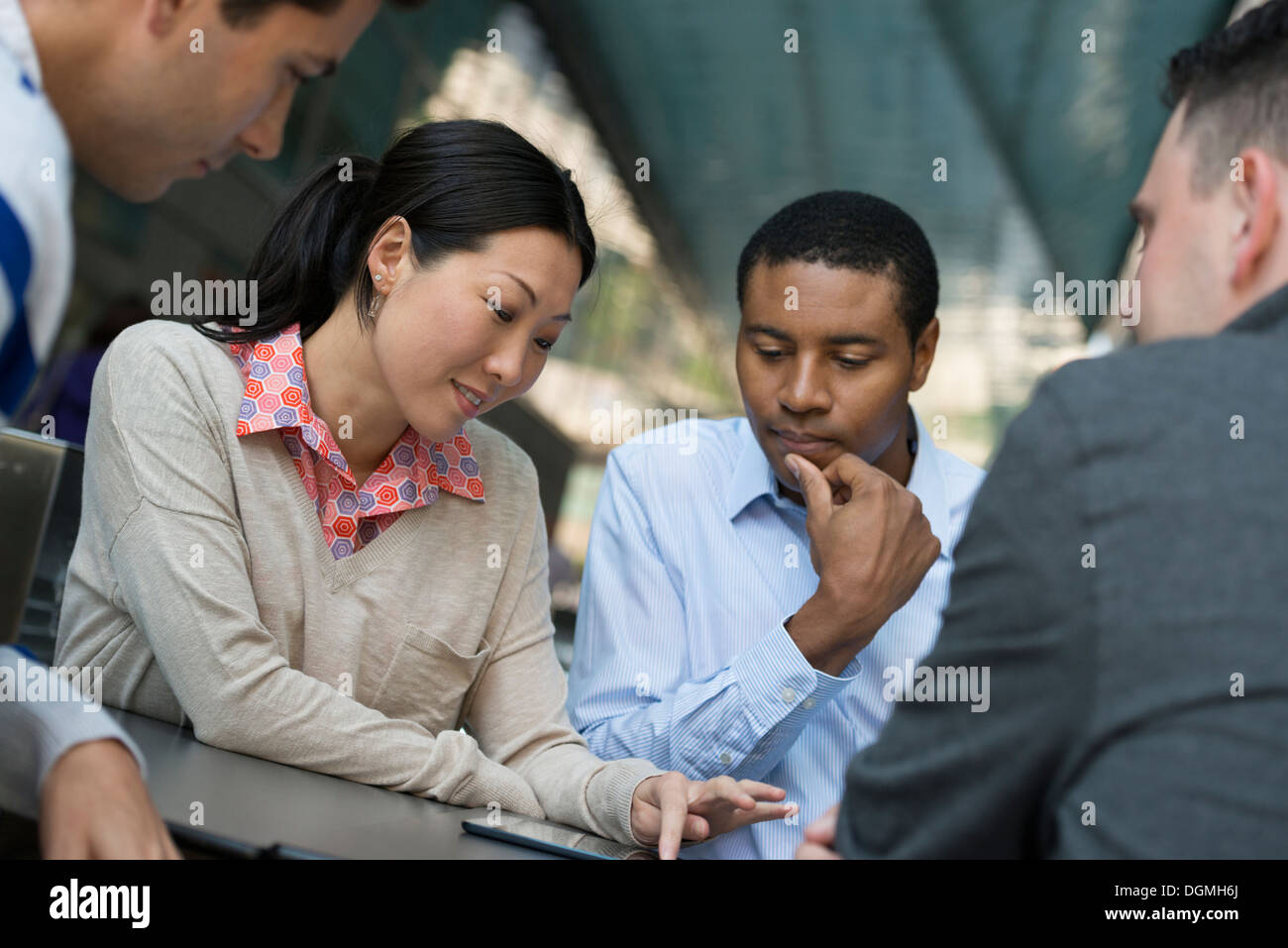 La gente di affari in movimento. Quattro persone raccolte intorno a una tavoletta digitale avente una discussione. Foto Stock