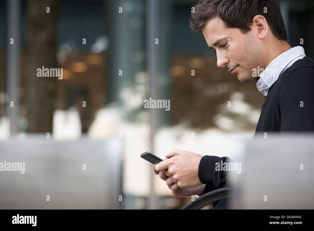 Estate in città. Un uomo seduto su un banco utilizzando un telefono intelligente. Foto Stock