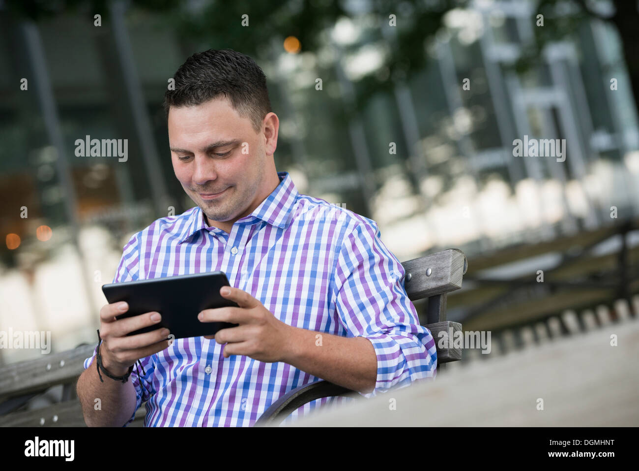 Estate in città. Un uomo seduto su una panchina utilizzando una tavoletta digitale. Foto Stock