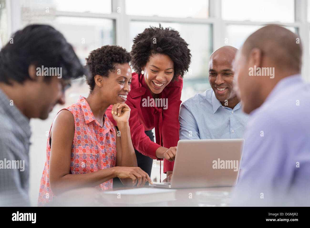 Vita in ufficio. Un gruppo di persone, uomini e donne in occasione di una riunione, usando un computer portatile. Foto Stock