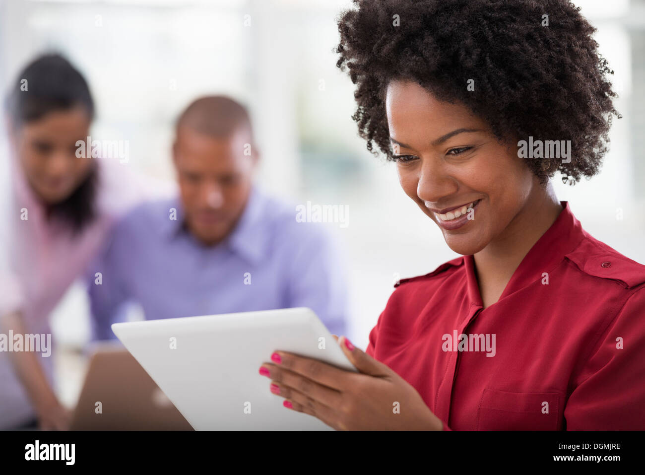 Vita in ufficio. Due persone in background e una giovane donna utilizzando una tavoletta digitale. Foto Stock
