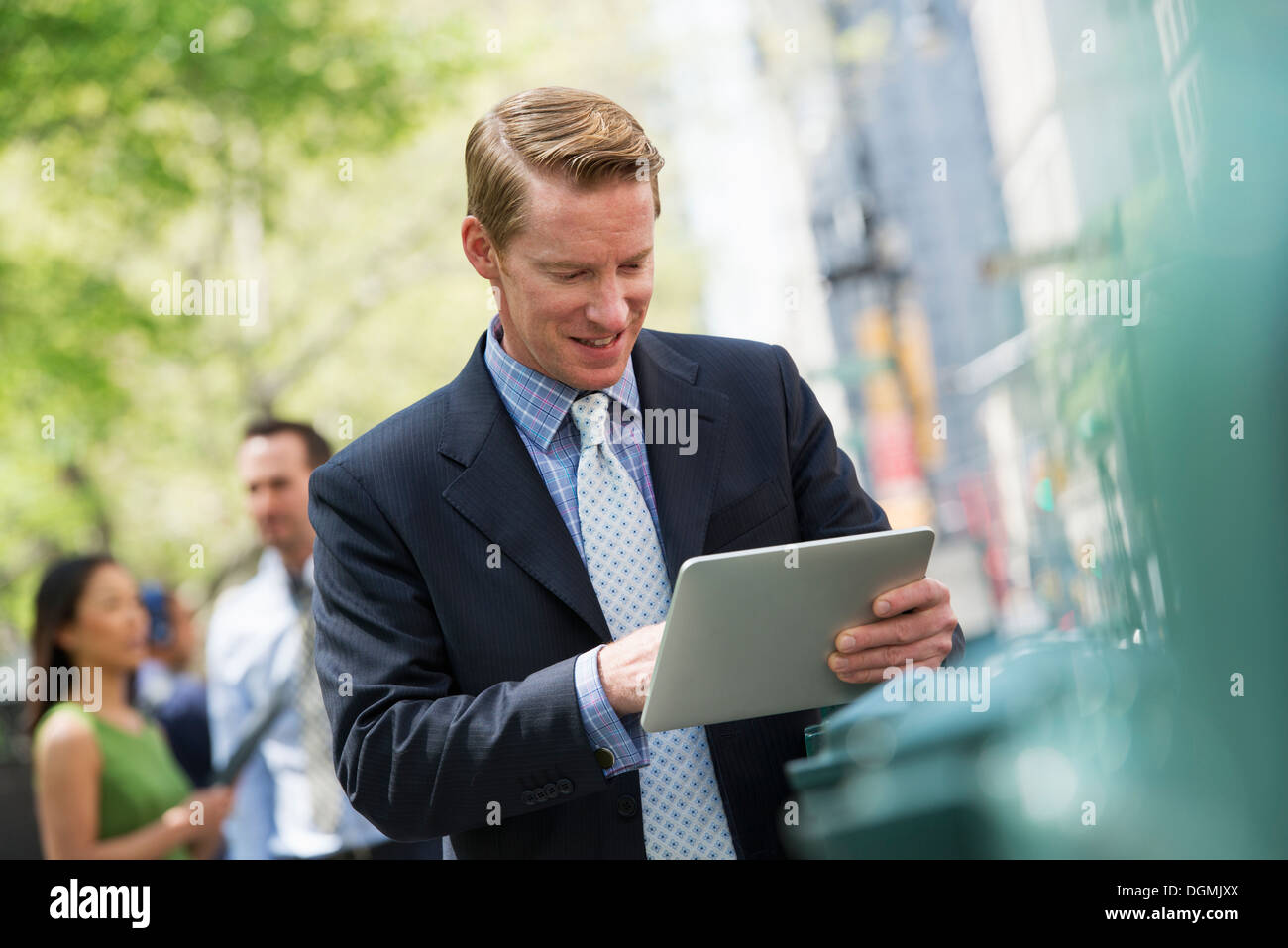 Tre persone di affari all'aperto nella città. Un uomo con una tavoletta digitale e un paio in background. Foto Stock