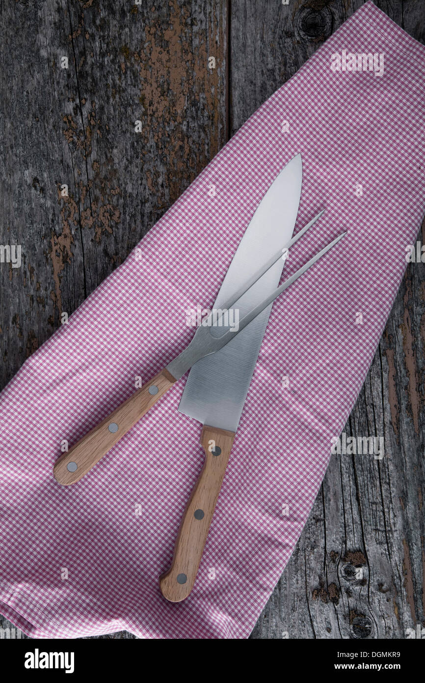 Il carving coltello e forchetta con un asciugamano da cucina rustica su tavole di legno Foto Stock