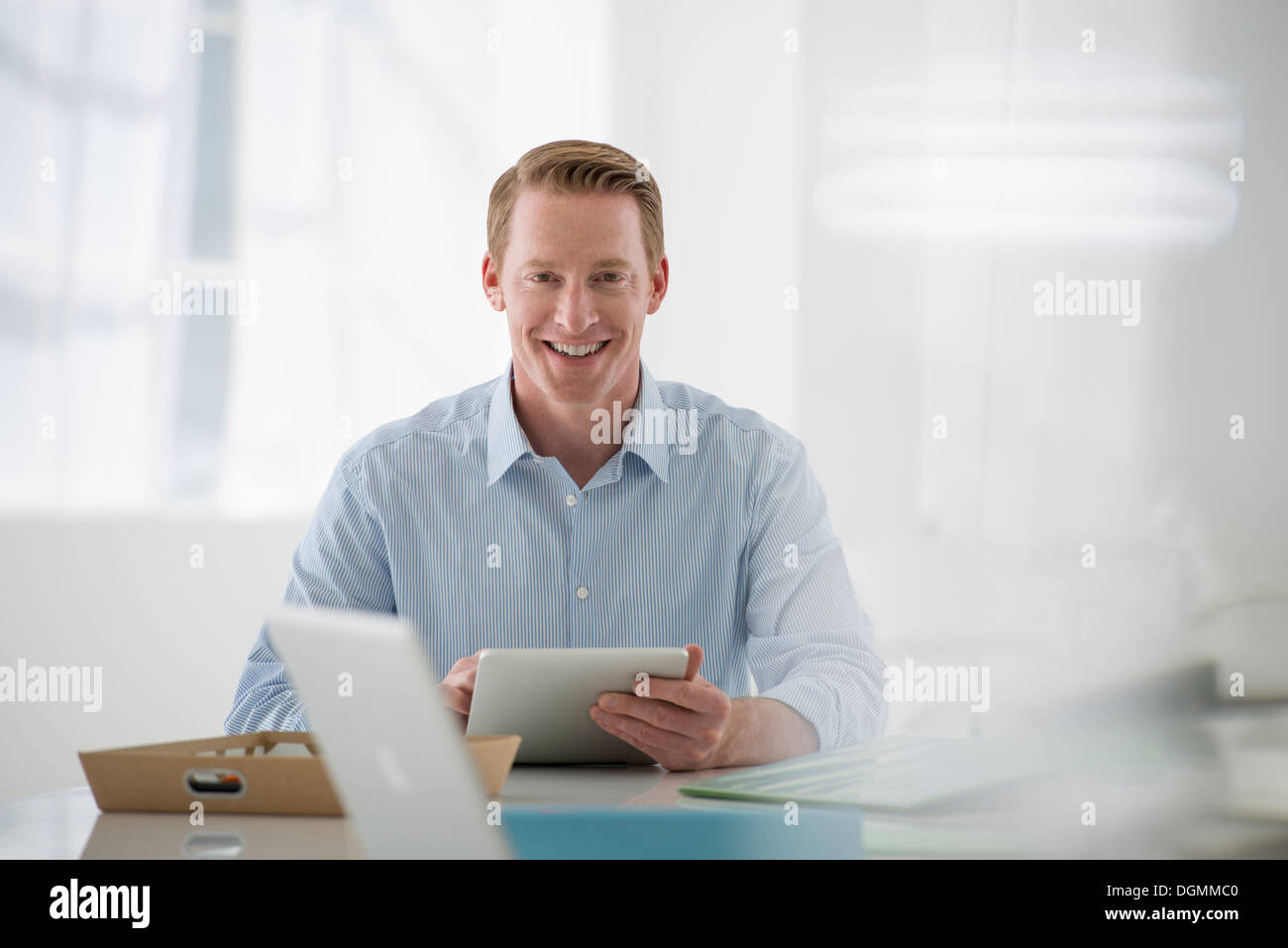 Business. Un chiaro e arioso ambiente office. Un uomo seduto in possesso di una tavoletta digitale. Foto Stock