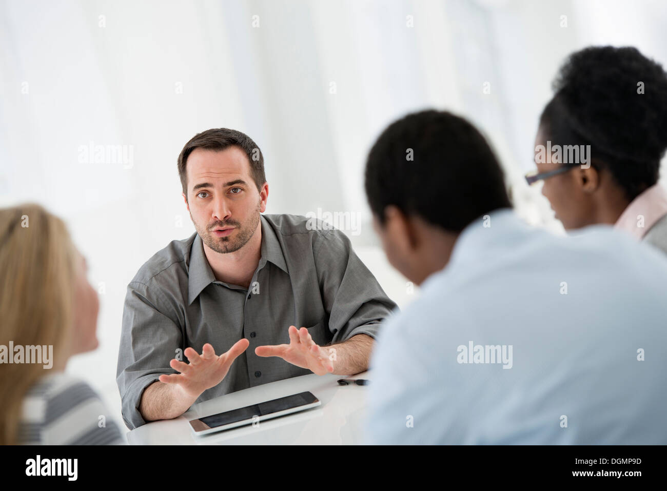 Ufficio interno. Un gruppo di quattro persone, due uomini e due donne, seduti attorno ad un tavolo. Riunione di affari. Foto Stock