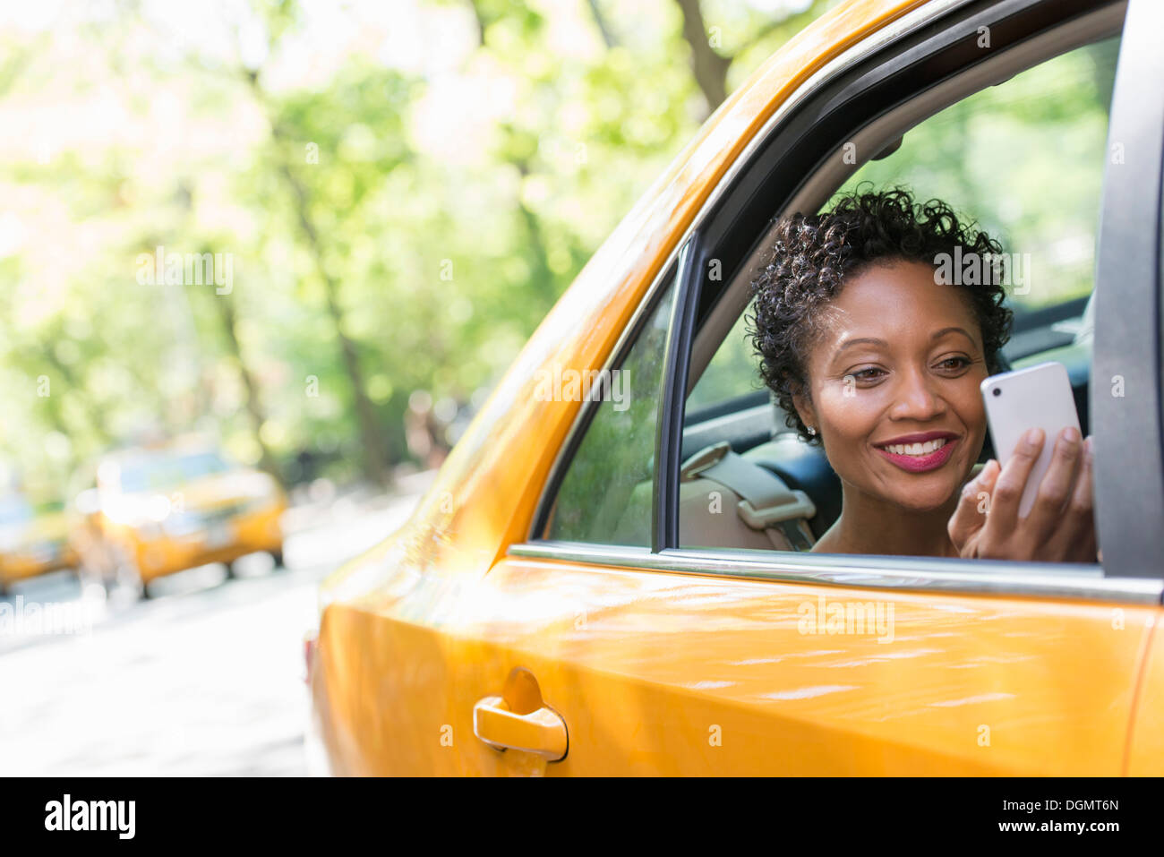 Una donna seduta nella parte posteriore del sedile passeggero di un taxi giallo, controllando il suo smart phone. Foto Stock