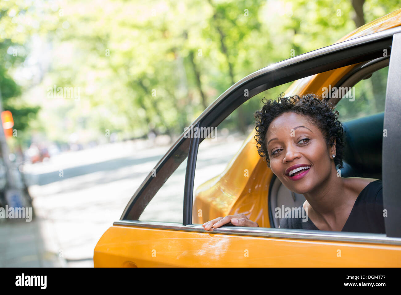 Una donna di uscire dalla parte posteriore del sedile passeggero di un taxi giallo. Foto Stock