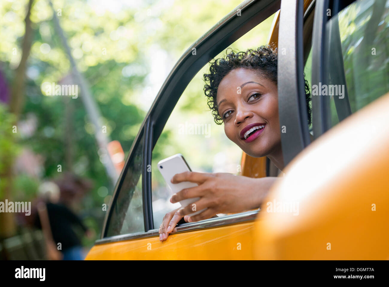 Una donna seduta nella parte posteriore del sedile passeggero di un taxi giallo, controllando il suo telefono. Foto Stock