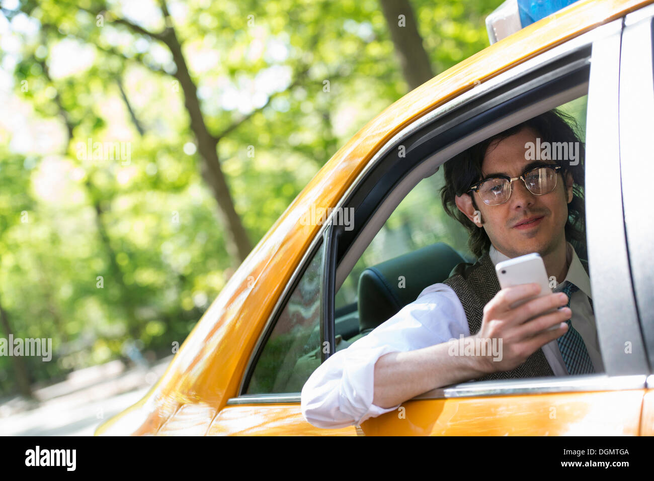 Un giovane uomo nel sedile posteriore di un taxi giallo, guardando il suo smart phone. Foto Stock