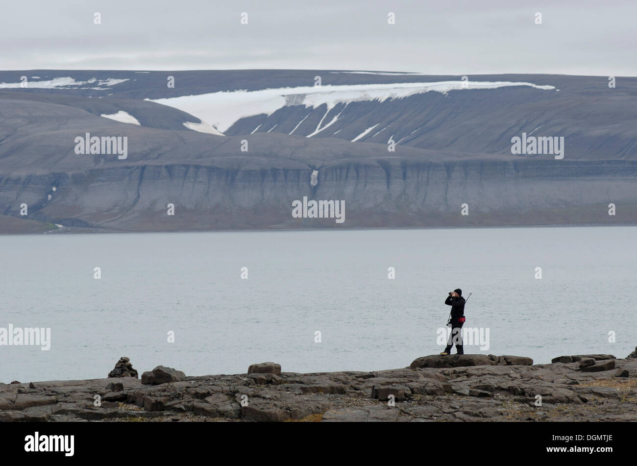 Persona con un fucile sopra la spalla guardando intorno con un binocolo per gli orsi polari, Freemansundet, Sundneset, Barentsøya Foto Stock